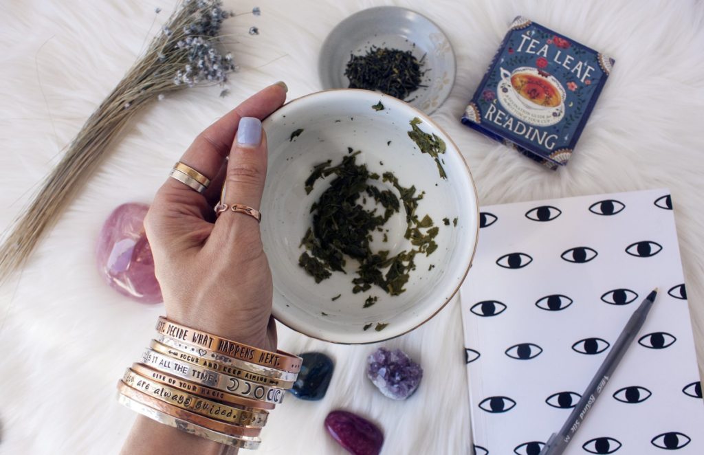 A woman wearing bangles is displaying tea leaves in a mug for a reading she has just completed.